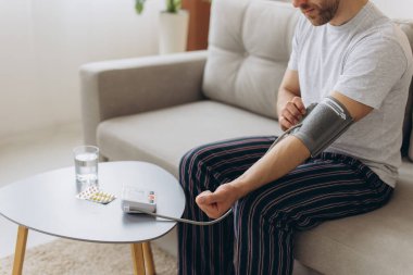 Evdeki kanepede oturan erkek, kan basıncını ölçüyor. Modern tonometre kullanan bir adam stresten kaynaklanan hipertansiyonu hisseder.