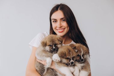 Beyaz arka planda Akita Inu yavrularını tutan mutlu gülümseyen bin yıllık kadının portresi