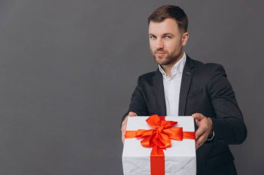 Sakallı mutlu gülen adam elinde bir hediye tutuyor ve gri arka planda, sevgililer gününde, Noel 'de ve yeni yıl konseptinde veriyor.