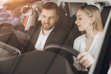 Becerikli araba satıcısı, kadın müşterilere lüks otomobilin içini gösteriyor. Beyaz adam ve kadın içeride oturup konuşuyorlar. Satma ve satın alma kavramı.