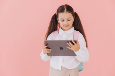 Eğitimde teknolojiyi kucaklayan genç bir ilkokul öğrencisi, canlı pembe bir arka plana karşı dijital tablet kullanıyor.