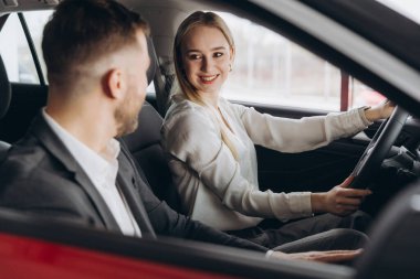 Becerikli araba satıcısı, kadın müşterilere lüks otomobilin içini gösteriyor. Beyaz adam ve kadın içeride oturup konuşuyorlar. Satma ve satın alma kavramı.