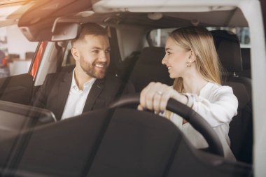Becerikli araba satıcısı, kadın müşterilere lüks otomobilin içini gösteriyor. Beyaz adam ve kadın içeride oturup konuşuyorlar. Satma ve satın alma kavramı.