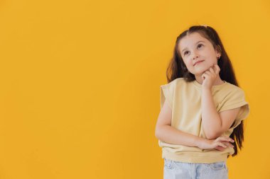 Uzun kahverengi saçlı, meraklı, meraklı, izole edilmiş sarı arka planlı küçük bir bayan.