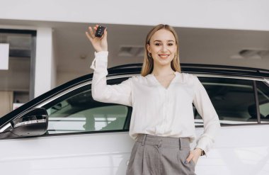 Mutlu Sahip. Yeni arabasının anahtarlarını elinde tutan neşeli beyaz bir kadın, Sevinçle Satış Merkezinde duran neşeli bir kadın, Kopyala Uzay