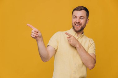 Sarı tişörtlü şirin adam sarı arka planda izole edilmiş fotokopi alanını işaret ediyor.