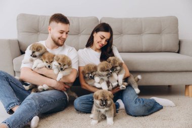 Güzel, gülümseyen mutlu çift köpek kulübesinde ya da barınakta Akia inu yavrularıyla oynuyor.