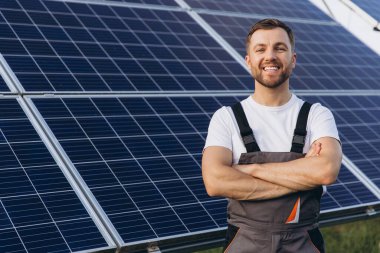 At the forefront of renewable energy innovation, smiling bearded male engineer stands with crossed arms, observing the efficient operation of a newly developed solar panel array clipart