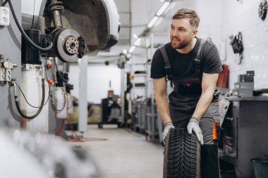 Happy Smiling Car mechanic working in garage and changing wheel alloy tire. Repair or maintenance auto service. clipart