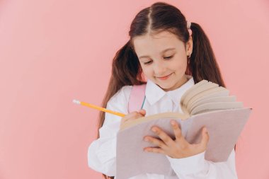 Okul üniformalı, sırt çantalı, kitap okuyan ya da pembe arka planda ödev yazan sevimli bir kız.
