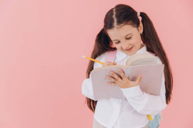 Okul üniformalı, sırt çantalı, kitap okuyan ya da pembe arka planda ödev yazan sevimli bir kız.