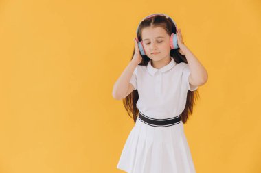 Kablosuz kulaklık takmış, dans eden, sarı duvarda izole bir şekilde müzik dinleyen sevimli beyaz çocuk.