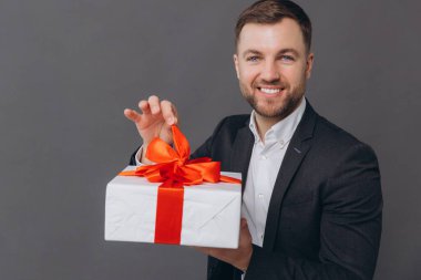 Sakallı mutlu gülen adam elinde bir hediye tutuyor ve onu gri bir arkaplanda açıyor. Sevgililer günü, Noel ve yeni yıl konsepti.