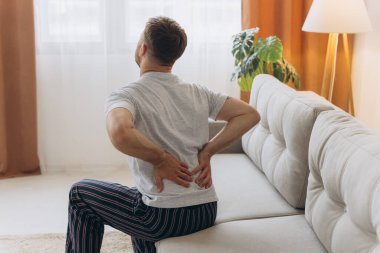 Beyaz pijamalı bir adamın sabahları evdeki koltukta oturması, sırtına dokunması, kas gerilmesinden muzdarip olması.