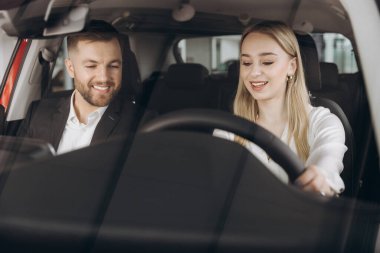 Becerikli araba satıcısı, kadın müşterilere lüks otomobilin içini gösteriyor. Beyaz adam ve kadın içeride oturup konuşuyorlar. Satma ve satın alma kavramı.