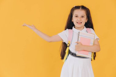 Sarı stüdyo arka planında poz veren mutlu bir okul kızının portresi.