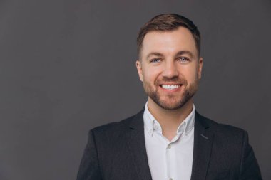 Bin yıllık beyaz iş adamının yakın plan portresi gri stüdyo arka planında izole edilmiş, resmi takım elbiseli başarılı bir erkek ve dişleriyle gülümsüyor.