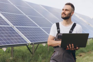 Makinist ya da inşaat işçisi sakallı adam güneş paneli durumunu kontrol etmek için dizüstü bilgisayar kullanıyor. Hücre santrali. Gelişmiş gerçeklik kavramı. Gelecekçi teknoloji