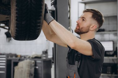 Yoğunlaştırılmış araba servisi çalışanının otomobil kontrol ekipmanlarına bakın. Üniformalı ve eldivenli erkek tamirci arabanın altında duruyor ve kırılma noktası arıyor.