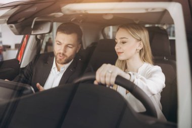 Becerikli araba satıcısı, kadın müşterilere lüks otomobilin içini gösteriyor. Beyaz adam ve kadın içeride oturup konuşuyorlar. Satma ve satın alma kavramı.