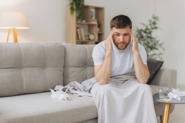 Ateşli ve baş ağrısı çeken hasta bir adam kanepede otururken başını tutuyor. Tedavi ve hastalık kavramı