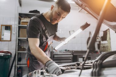 Araba servisi, onarım, bakım ve insan konsepti. Lambalı tamirci atölyede çalışıyor.