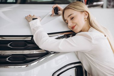 Bayilikte yeni arabasına sarılan olumlu, genç, beyaz bir kadın. Mutlu kadın sonunda uzun zamandır beklenen arabaya kavuştu.