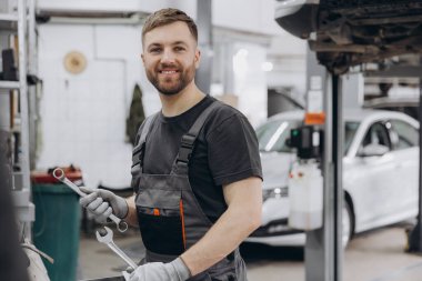 Araba tamircisinin elinde İngiliz anahtarı ve araba servisi geçmişinde anahtar bir araç var.