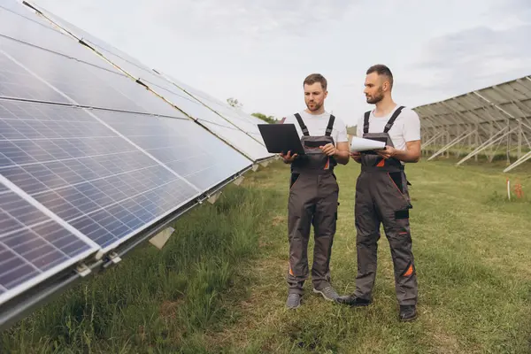 Güneş paneli inşaatının verimliliğini kontrol etmek için dijital tablet okuma bilgisi kullanan bir enerji uzmanı. Yeşil enerji işleri. Teknoloji. İki güneş enerjisi santrali işçisi veri kaydediyor