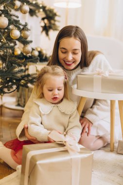 Mutlu anne ve kız Noel hediyelerini dekore edilmiş bir Noel ağacının yanında açıyorlar, birlikte bayram sezonunun tadını çıkarıyorlar.