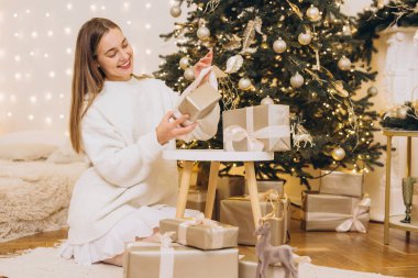 Güzel dekore edilmiş bir Noel ağacının altında Noel hediyelerini düzenleyen genç bir kadın sıcak ve şenlikli bir atmosfer yaratıyor.