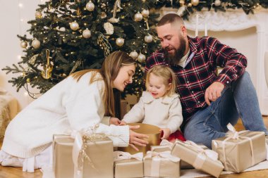Gülümseyen aile noel hediyelerini açarken süslü Noel ağacının yanında, kış tatillerinin tadını çıkarırken.