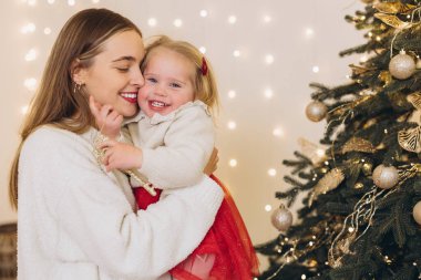 Anne ve kızı, güzel dekore edilmiş bir Noel ağacının yanında güzel bir anı paylaşıyor, neşeli atmosferin tadını çıkarıyorlar.