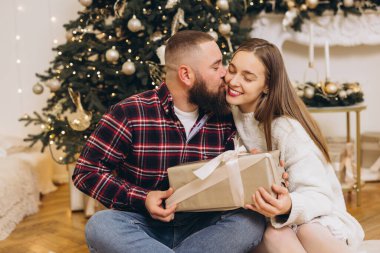 Mutlu çift, evdeki süslü Noel ağacının yanında otururken hediyelerini değiş tokuş ediyorlar.