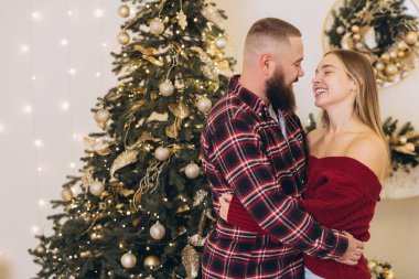 Sakallı adam ve sarışın kadın Noel ağacının yanında sarılıp Noel arifesinin tadını çıkarıyorlar.