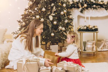 Anne ve kızı Noel hediyelerini dekore edilmiş bir Noel ağacının yanında değiş tokuş ederek sıcak ve şenlikli bir ortam yarattılar.