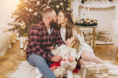 Anne babalar Noel ağacının yanında kızlarıyla otururken birbirlerini öpüyorlar ve hediyeler veriyorlar.