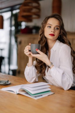 Genç iş kadını kafede kitap okurken bir fincan kahvenin keyfini çıkarıyor, işe ara veriyor.