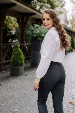 Sonbahar sezonu boyunca kırmızı rujlu, gülümseyen ve şehir sokaklarında yürüyen bir iş kadını.