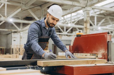 Marangoz, bir modüler yapı fabrikasında ahşap bir tahtanın ölçümlerini alıyor, prefabrik inşaatı için kesin kesintiler sağlıyor.