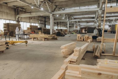 Geniş bir endüstriyel atölyeye yerleştirilmiş kereste yığınları işleme ve montajı bekliyor.