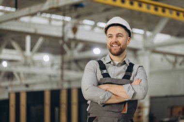Modüler yapı fabrikasında gülümseyen çapraz kollu kendinden emin mühendis prefabrik inşaatlarda uzmanlık ve profesyonellik sergiliyor.