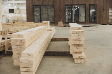 Bir fabrika içindeki modüler bir binanın bileşenleri olarak numaralandırılmış kereste yığınları montaj için hazır bekliyor.