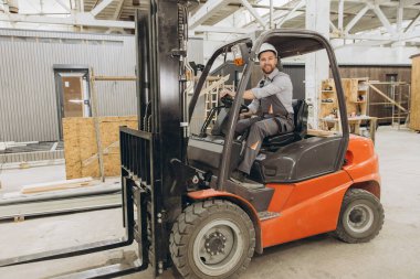 İnşaat işçisi fabrikada forklift kullanıyor prefabrik modüler binalar üretiyor, lojistik ve malzeme işleme işleriyle uğraşıyor.