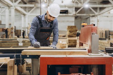 Marangoz, büyük bir marangozluk atölyesinde prefabrik ev inşaatı üzerinde çalışarak ahşap bir kalas üzerinde ölçümler yapıyor.