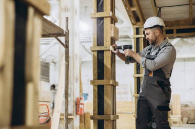 Modüler yapı fabrikasında elektrikli tornavida kullanarak prefabrik ev sütunlarını monte eden inşaat işçisi.