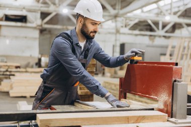 Koruyucu giysili marangoz, yoğun bir atölyede testereyle odun keser. İnşaatta ustalık ve hassasiyet sergiler. İşçi ustalığını ve güvenliğini gösterirken talaş uçar.