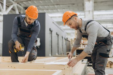 İki marangoz bir atölyede ahşap bir çerçeve üzerinde çalışarak modüler konutlar için prefabrik bileşenler oluşturuyorlar.