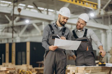 İki müteahhit planları inceliyor ve bir modüler yapı fabrikasında prefabrik parçaları monte etmeye hazırlanıyor.