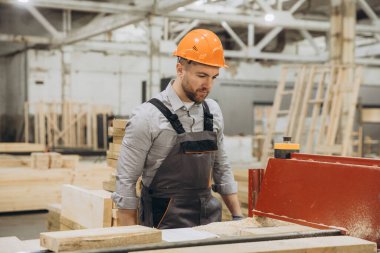 Marangoz, prefabrik ahşap evler üreten bir fabrikada işçi tulumu giyer ve şapka takar.